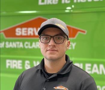 Young man looks smiling towards the camera in front of SERVPRO van