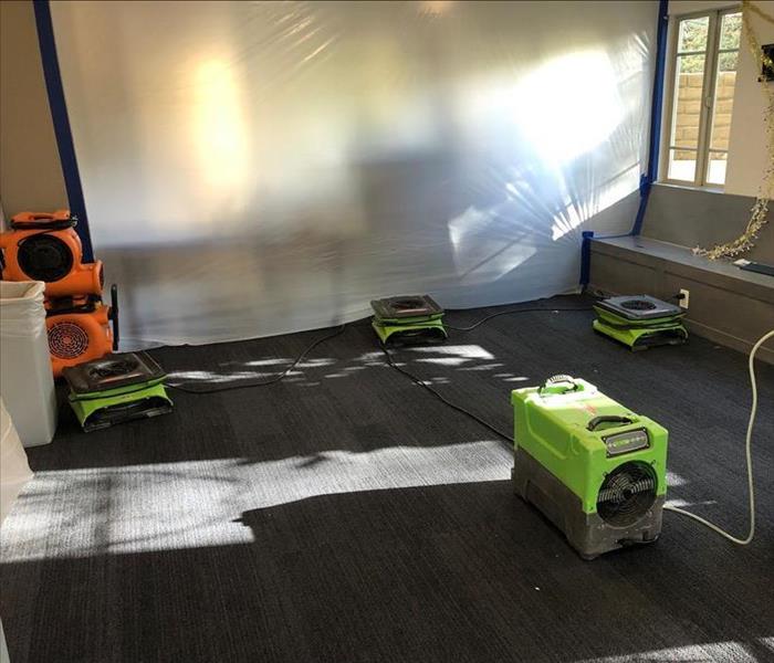 Centrifugal air movers in the corner while stackable air movers and dehumidifiers dry water damage in a partially sealed room