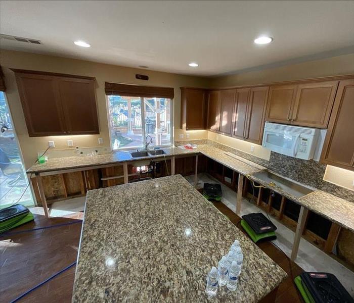 Open kitchen with removed cabinetry and lower drywall with four SERVPRO air movers operating nearby